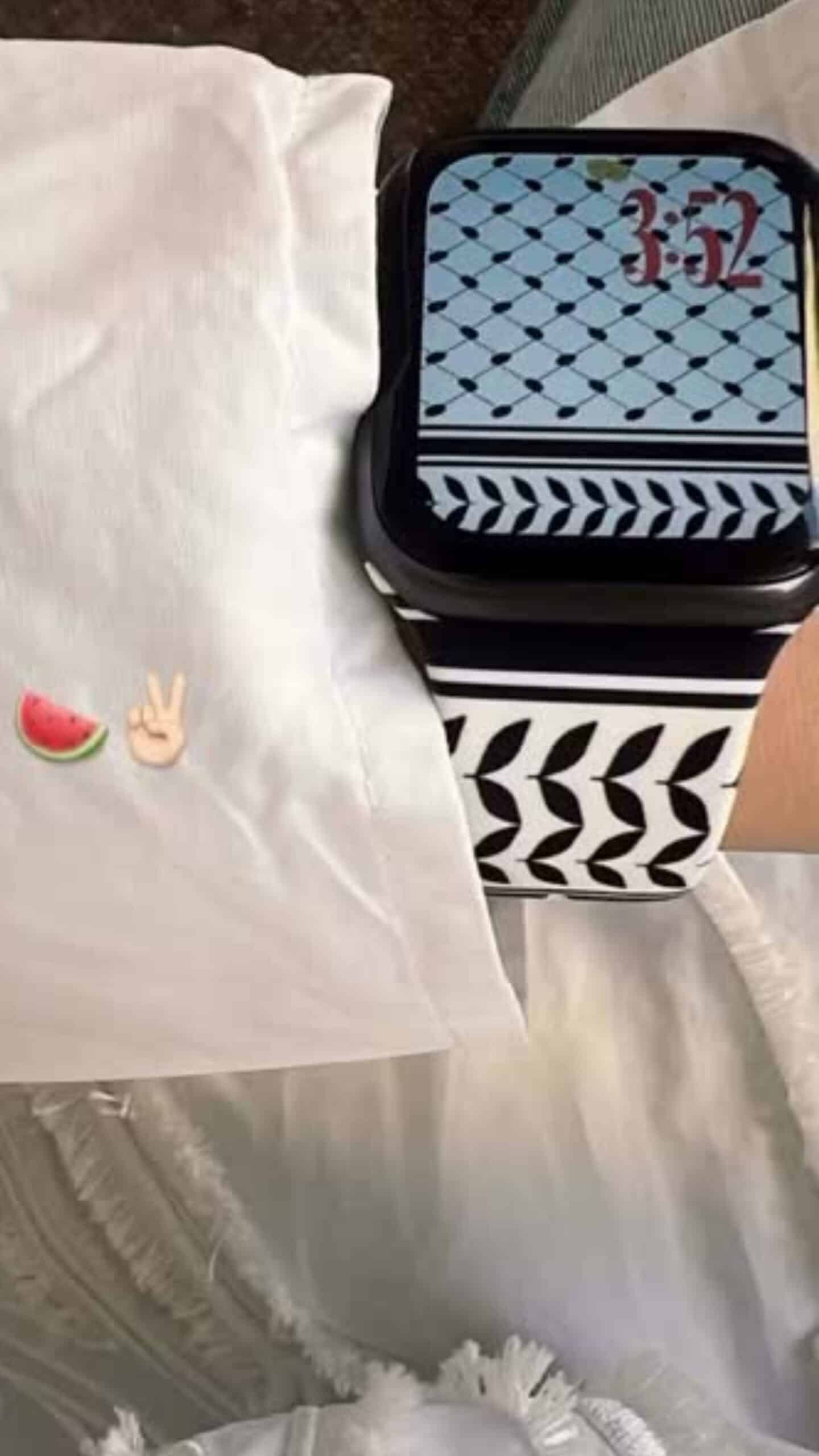 Smartwatch showing time 3:52 on stylish black and white band, placed on white bed with watermelons and peace hand emoji.