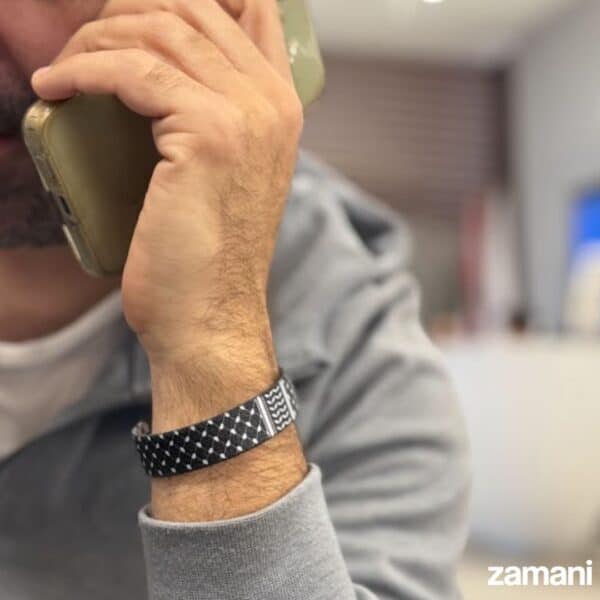 Stylish black and white patterned bracelet on man's wrist, holding a smartphone, casual gray hoodie.
